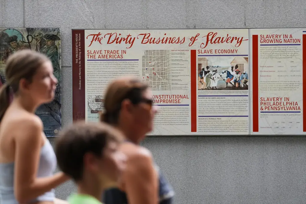 People walk past an informational panel at President’s House Site...