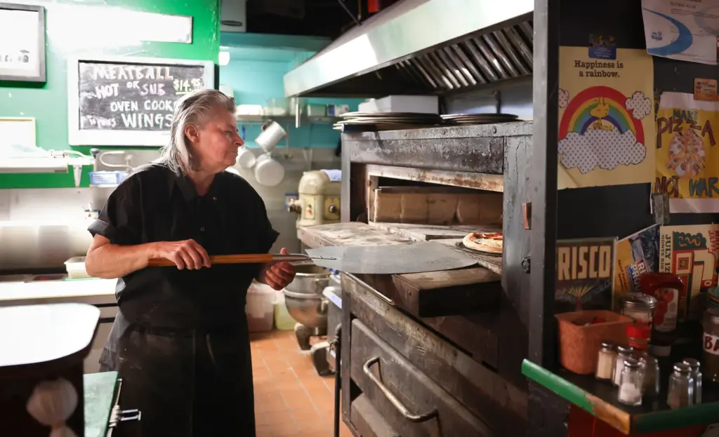 Suzy Kuhr checks on a pizza in the oven at...
