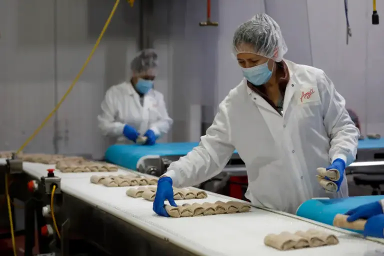An employee places bean and cheese burritos on a conveyor...