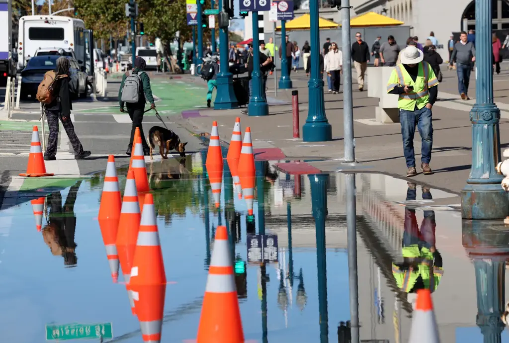 People walk past high tide flooding along the Embarcadero in...