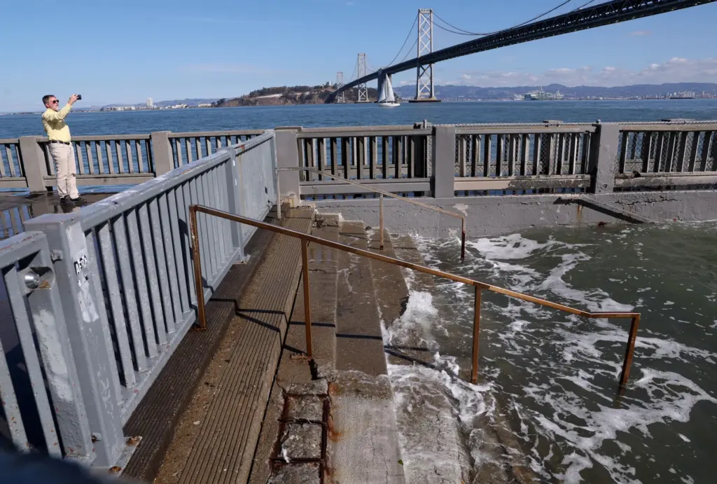A man photographs high tide flooding along the Embarcadero in...