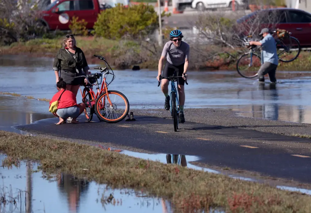 Bicyclists make their way through high tide flood waters on...