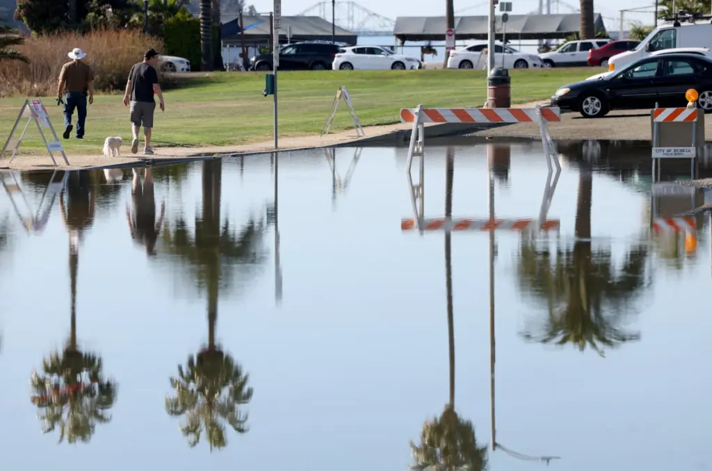 People walk past igh tide flooding along East B Street...