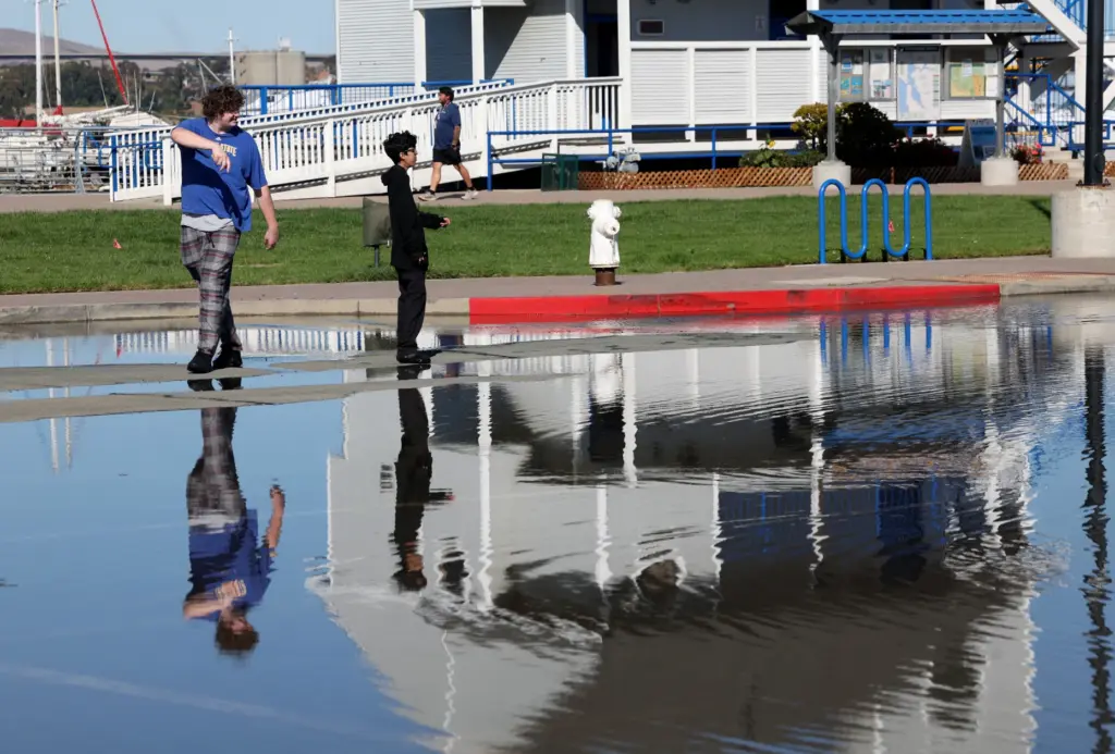 People walk past high tide flooding at the Martinez Marina...